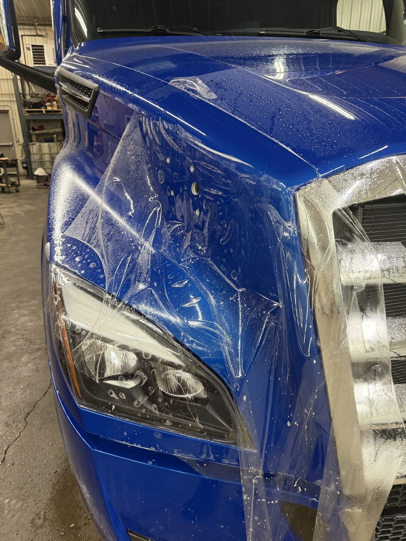 Clear paint protection film being fitted to a blue truck hood and fender